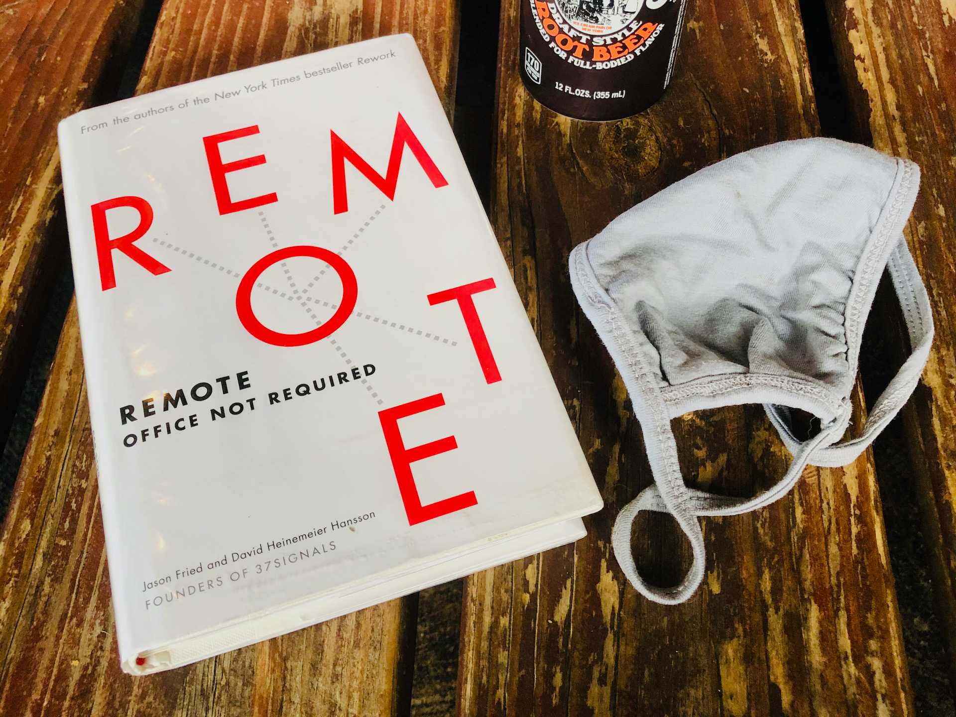 Remote: Office Not Required hardcopy book on a table and a gray cloth face mask to the right